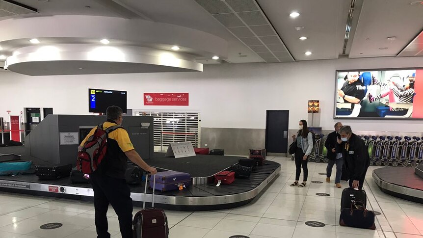 People wait around an airport carousel for luggage.