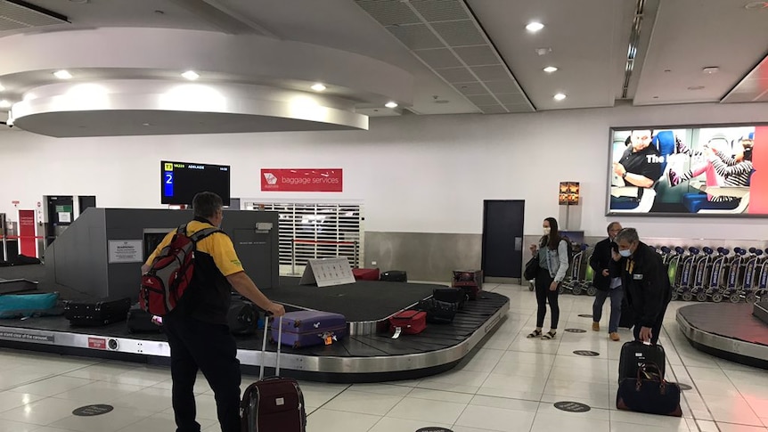 People wait around an airport carousel for luggage.