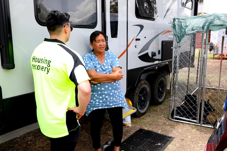 A woman stands in front of her caravan talking to a Housing Recovery worker.