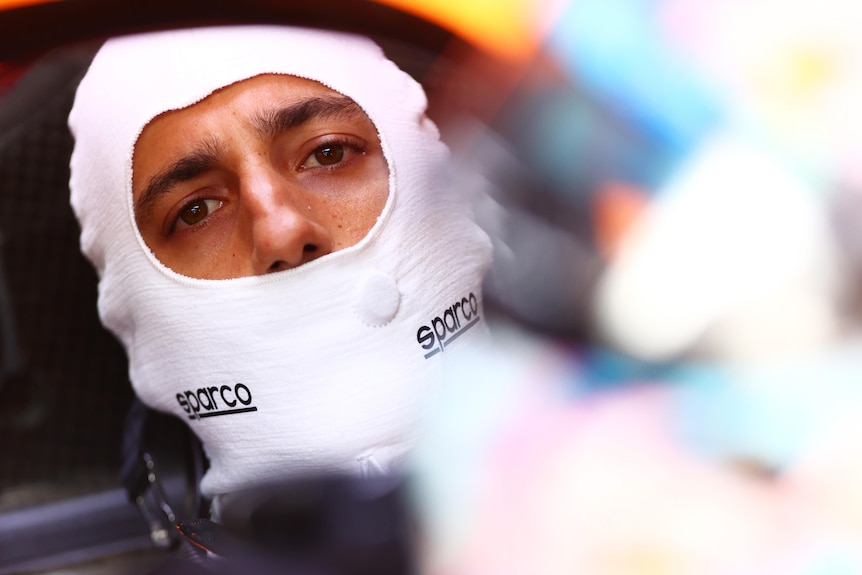 Race car driver sitting in his car with a balaclava on.