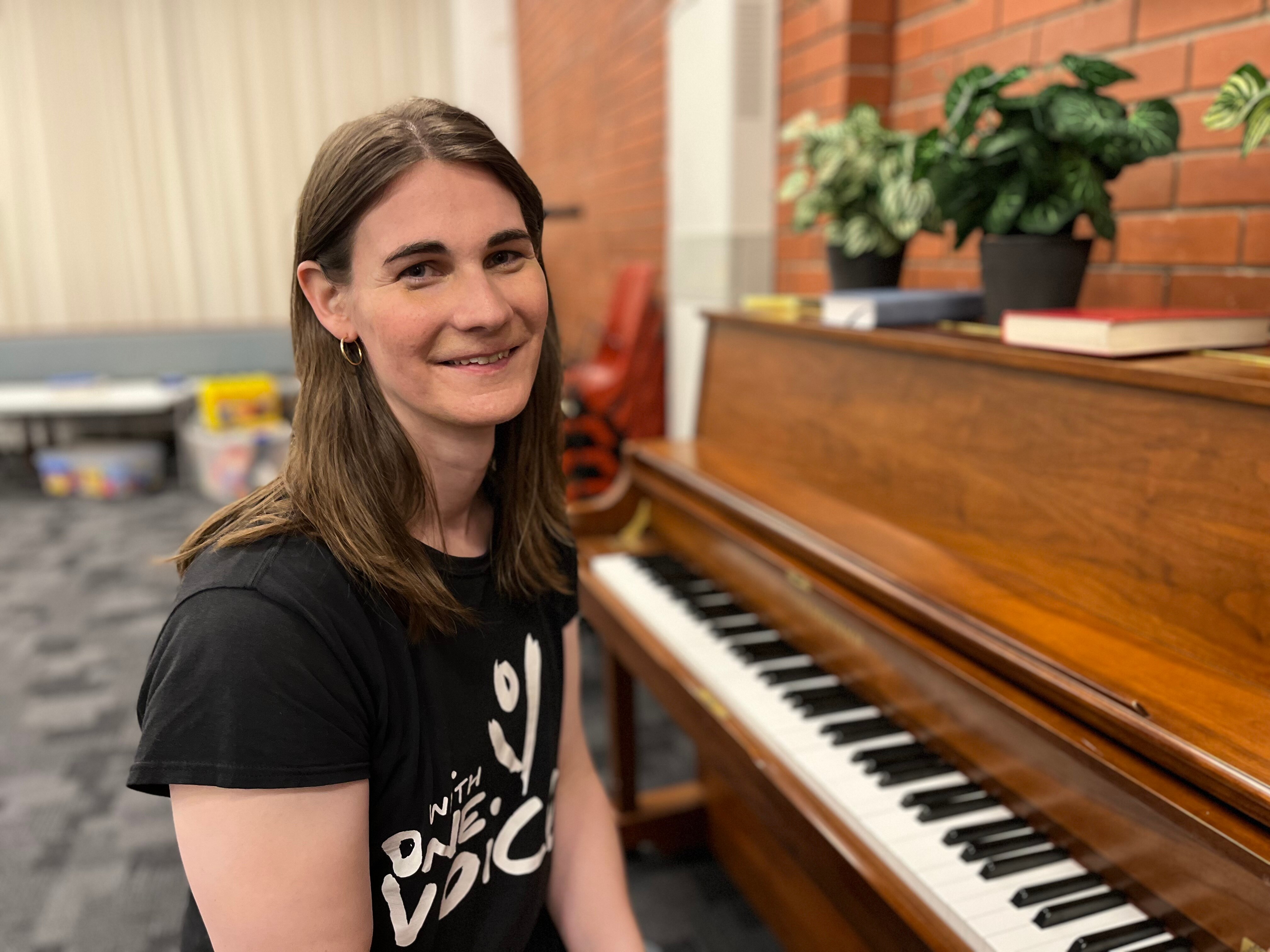 Woman with long brown hair smiles while sitting at a piano