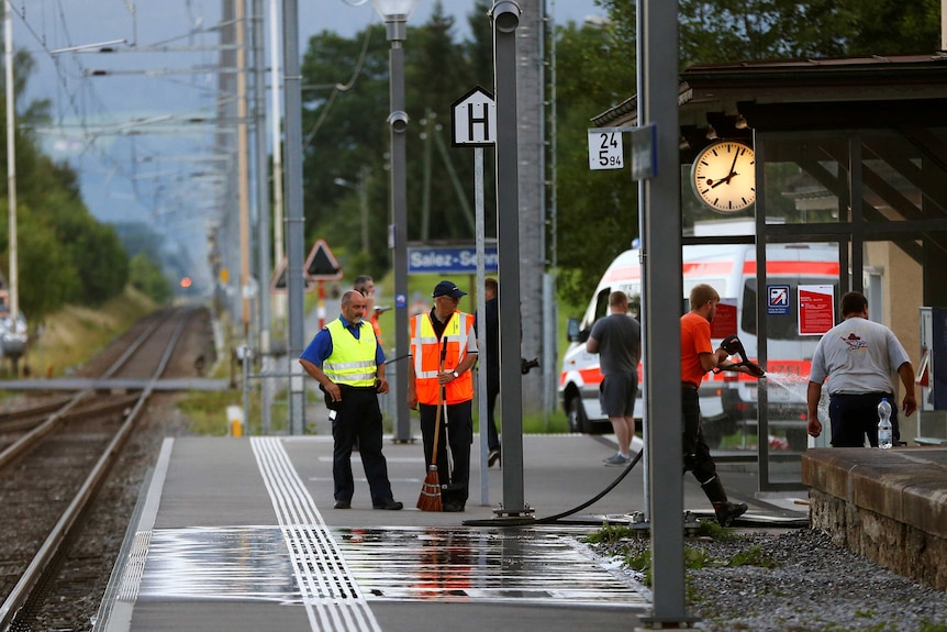 A Swiss police officer stands near workers cleaning a platform.