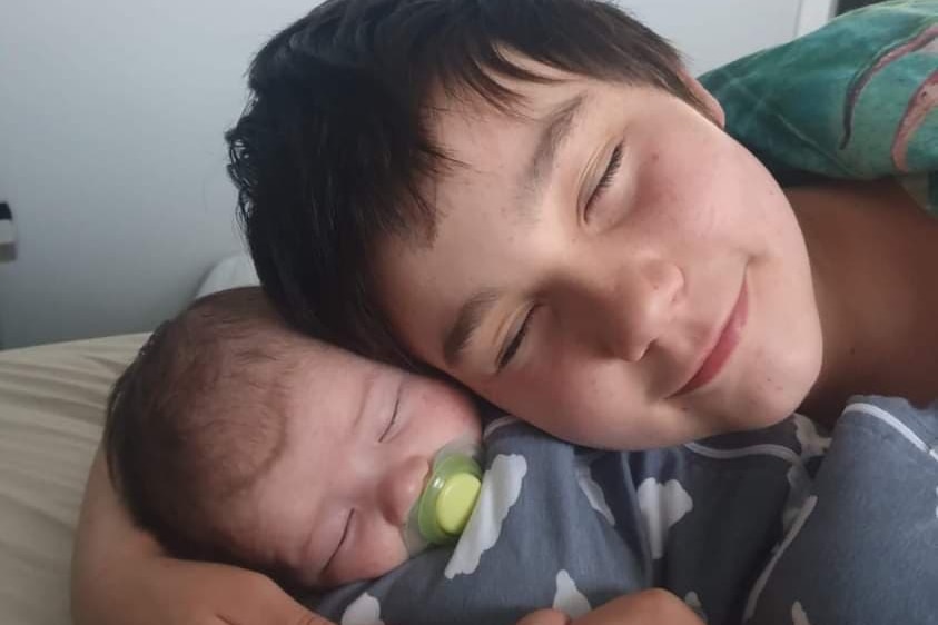 A young boy cuddles a baby, both with their eyes closed