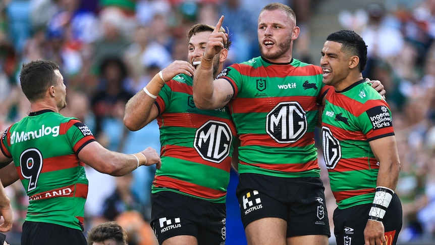 A South Sydney NRL player points his finger in celebration as he stands next to teammates after a try.