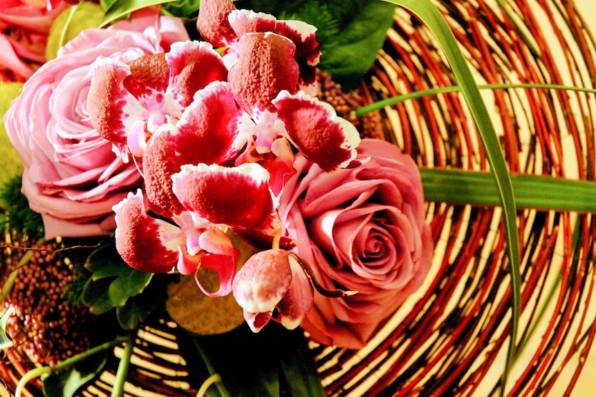 Orchids and pink roses come together on a basket of native grass.