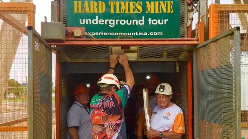 A man, holding the Queen's Relay Baton, with two other men gets ready to go a mine shaft.