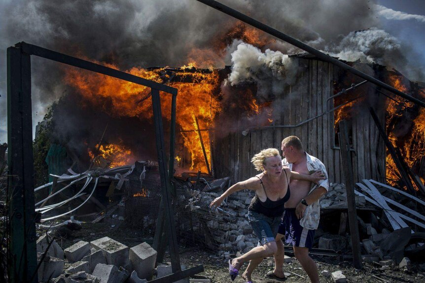 Civilians escape from a fire at a house destroyed by an air attack in the Luhanskaya village.