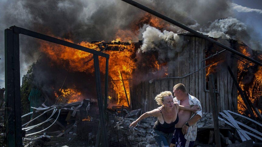 Civilians escape from a fire at a house destroyed by an air attack in the Luhanskaya village.