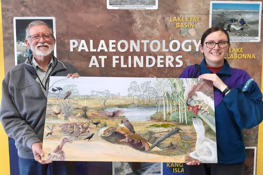 A man and woman hold up a large painting 