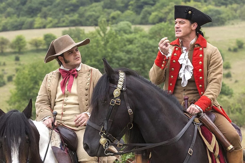 Beauty and the Beast characters Lefou and Gaston ride horses in a scene from the film.