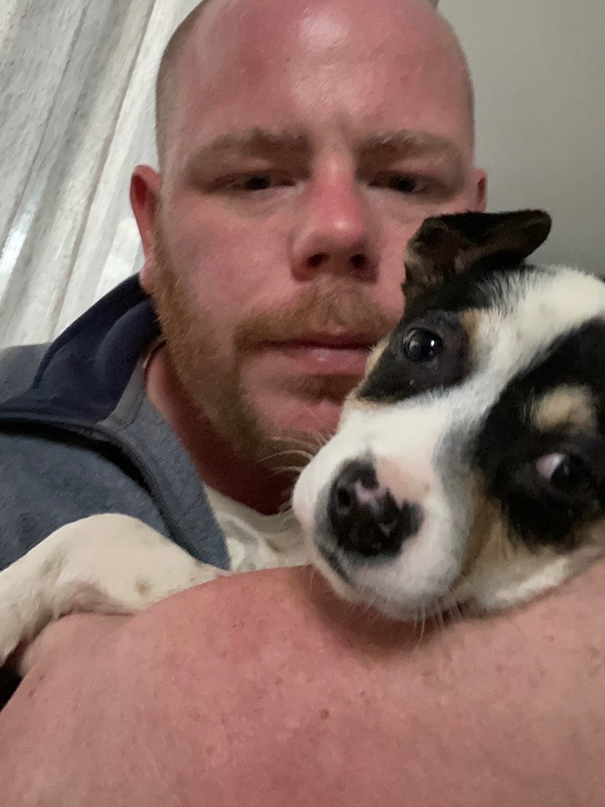 A man cuddles a small puppy which is coloured white., black and tan.