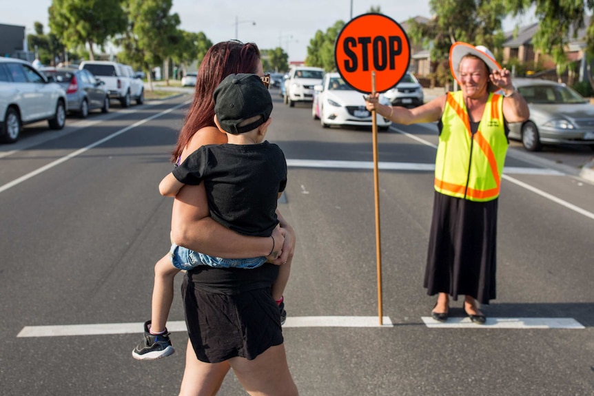 Kristie Ferraro crosses the road in Mernda, with the assistance of the local lollypop lady.