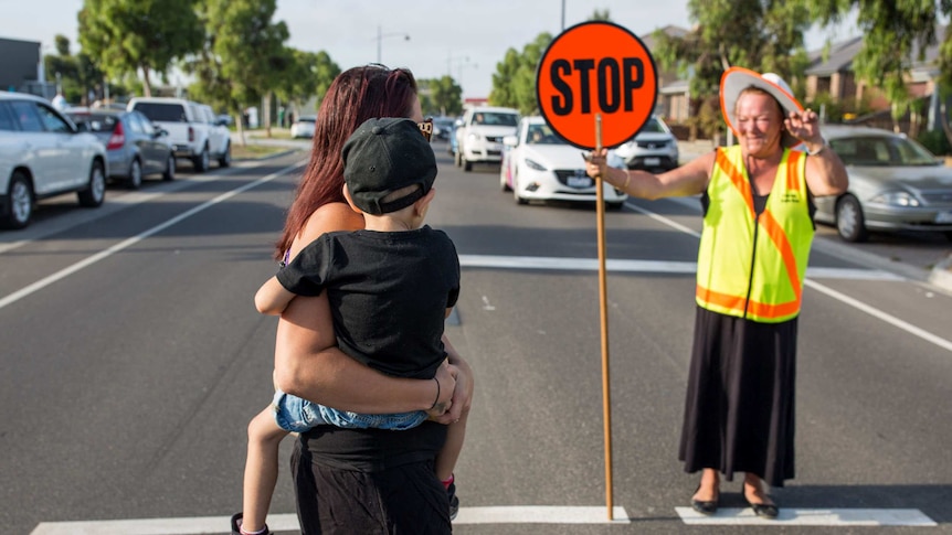 Kristie Ferraro crosses the road in Mernda, with the assistance of the local lollypop lady.