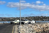 Two police cars and one ambulance at the end of the road next to the sea
