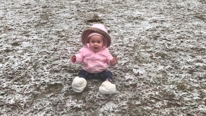 Elsie Willett sitting in a field of light snow in a pink puffer hoodie.
