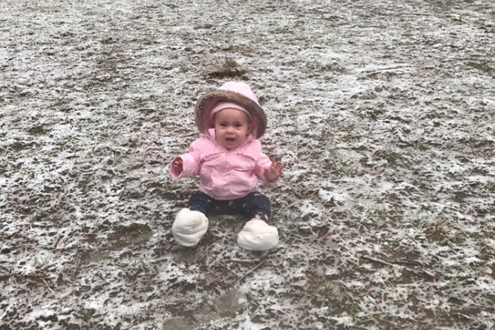 Elsie Willett sitting in a field of light snow in a pink puffer hoodie.