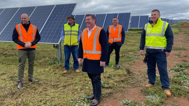 Five men in bright vests stand near a solar farm.