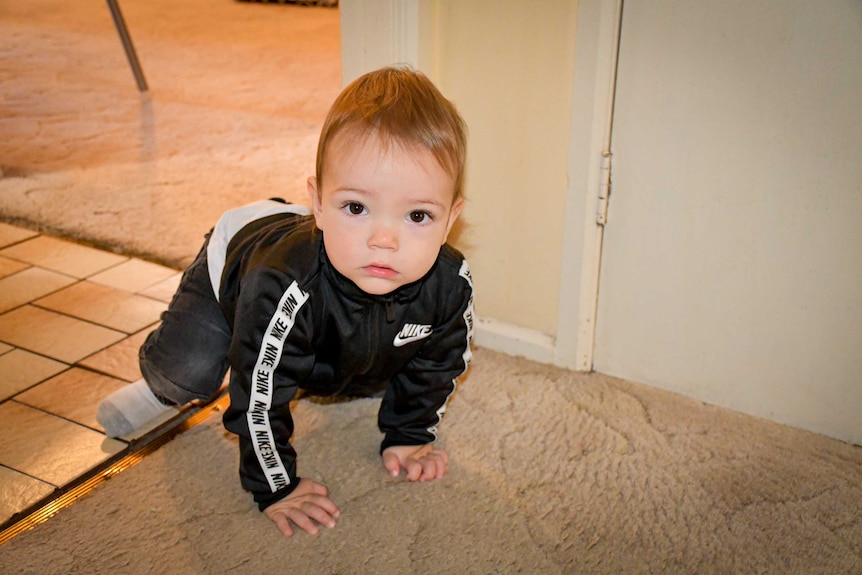 A small boy in a nike tracksuit crawls along the floor.