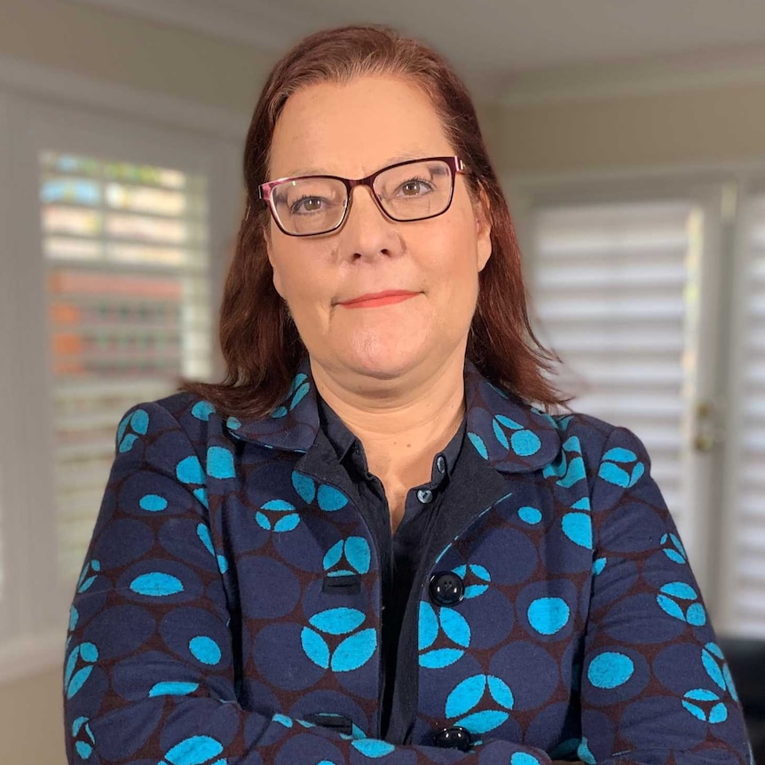 Economist Nikki Hutley stands with arms folded in front of windows at her home.