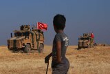 A boy holding a stick watches as a convoy of Turkish-flagged armoured vehicles drives past.