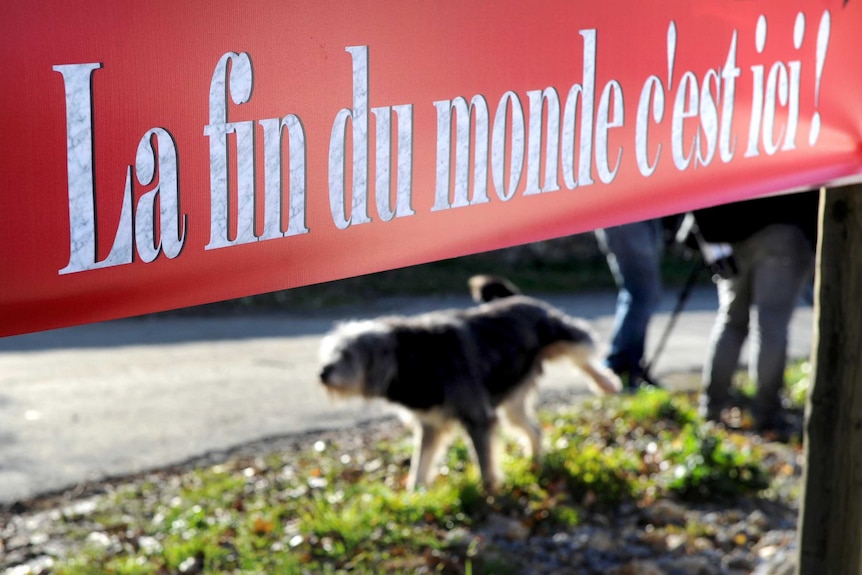 A dog in the town cocks its leg under a sign reading 'The end of the world is here'.