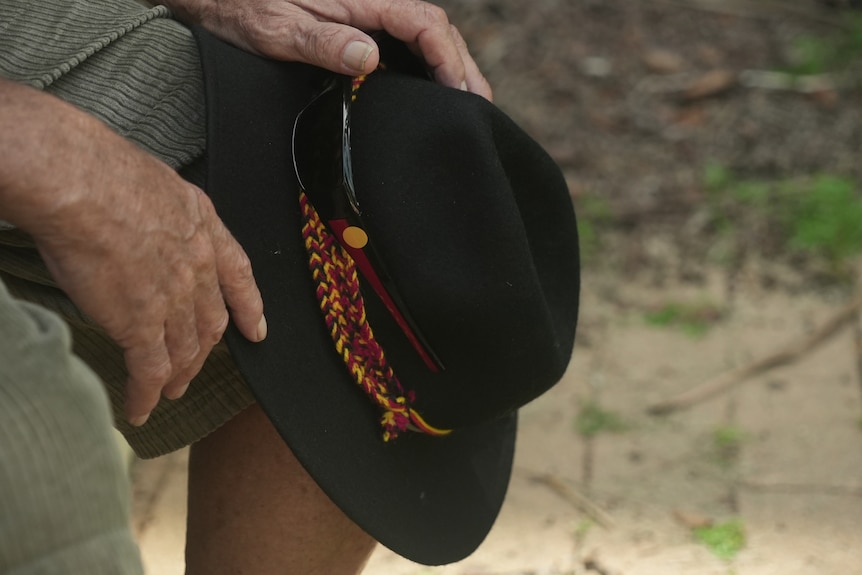 A close-up of man holding a hat with the colours of the Aboriginal flag.