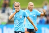 A female soccer player wearing light blue holds her hand to her mouth in surprise