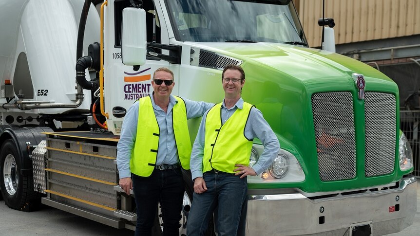 Two men standing in front of a cement truck.