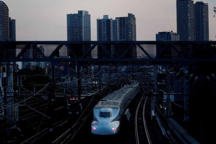 A bullet train heads into downtown Tokyo with the sillouette of the city behind it.