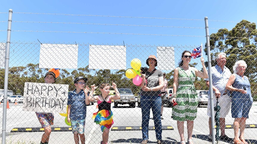 A small group of well-wishers hold a Happy Birthday sign for Prince Charles against wire fencing at Albany airport.