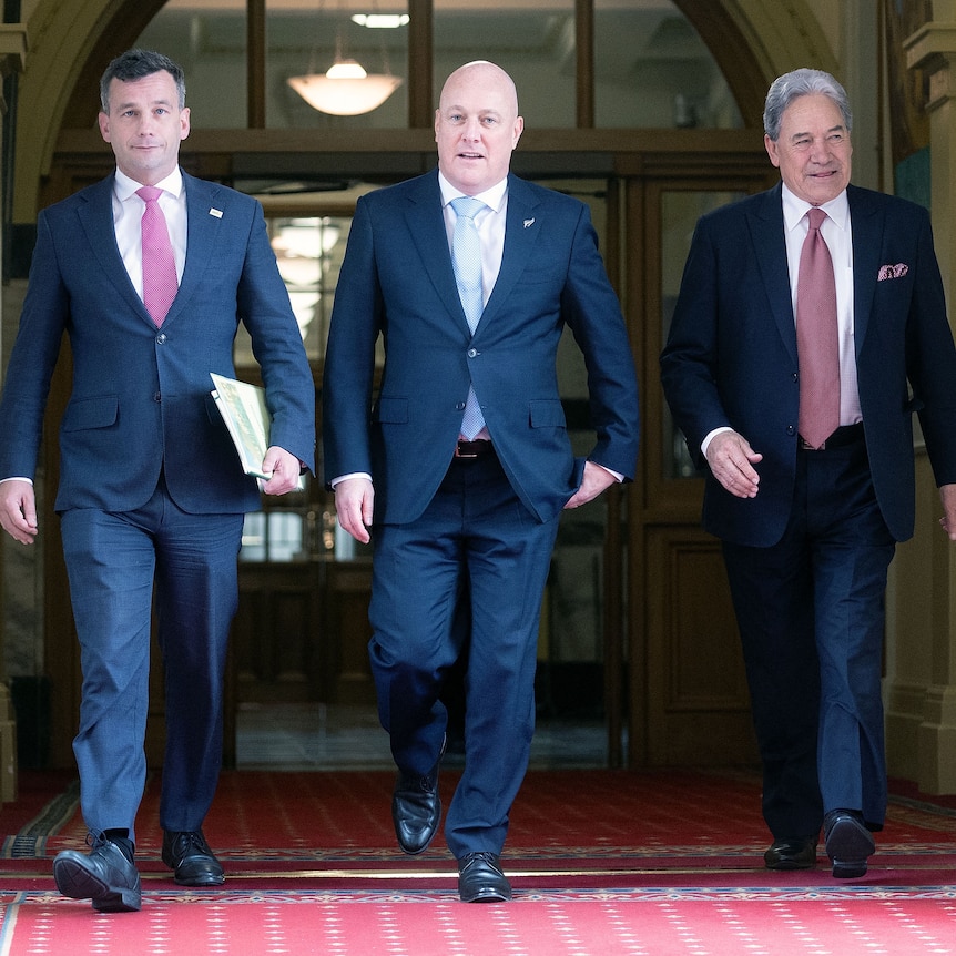 Three men in suits walk in a corridor
