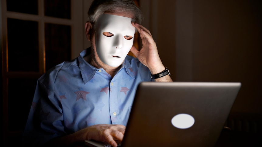 A man with a face mask is sitting behind a desktop computer