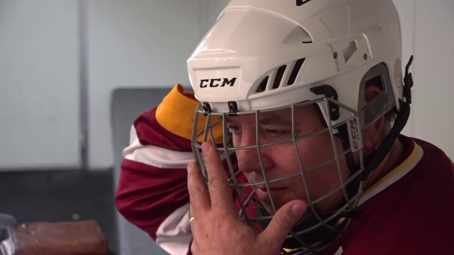 Um homem colocando um grande capacete branco com um escudo de metal para proteger o rosto.