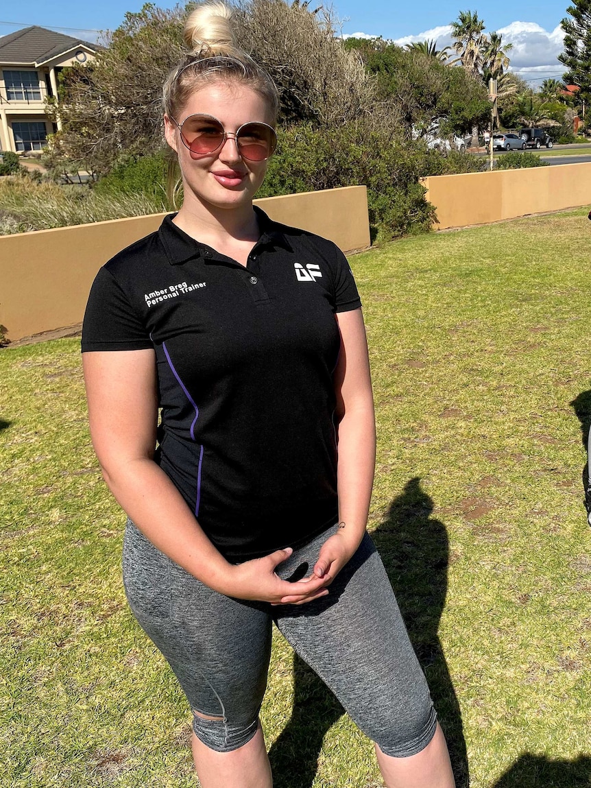 A woman with sunglasses on stands on a lawn smiling at the camera.