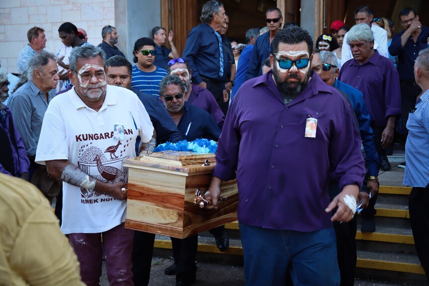 Several men carrying a coffin as they walk out of a church at a funeral service.