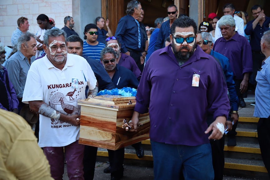 Several men carrying a coffin as they walk out of a church at a funeral service.