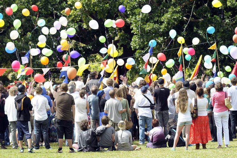 A group of mourners at a funeral release a bunch of balloons