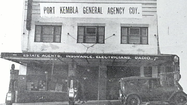 Wide black and white archive shot of a shopfront in the early 1900s.