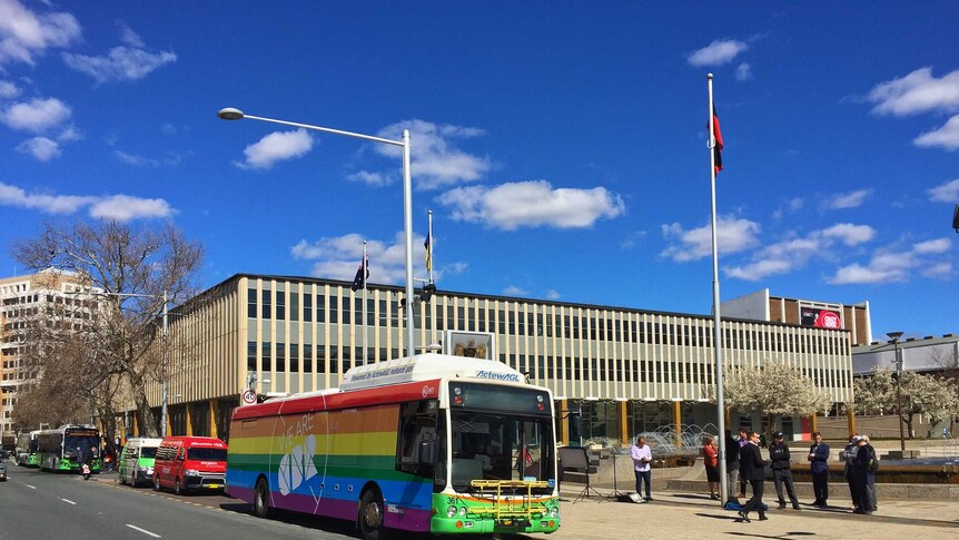 Rainbow coloured bus parked in the street outside of building