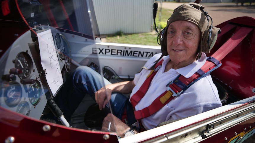 An elderly pilot sits in the cockpit of a plane.