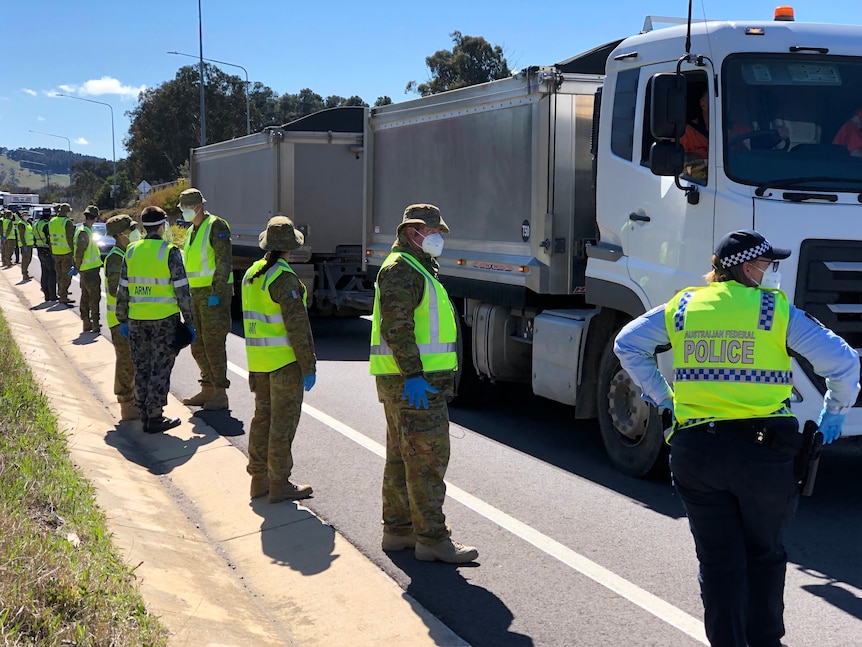 A line of people in high-visibility jackets on the side of a highway. Most are wearing Army camouflage uniforms underneath.