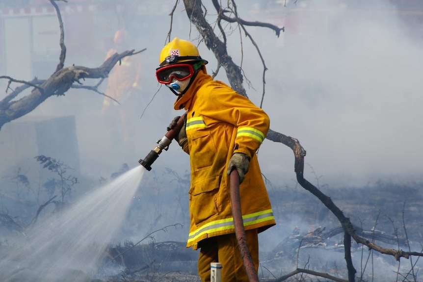 A CFA firefighter, wearing goggles and breathing mask and hose in smoky area.