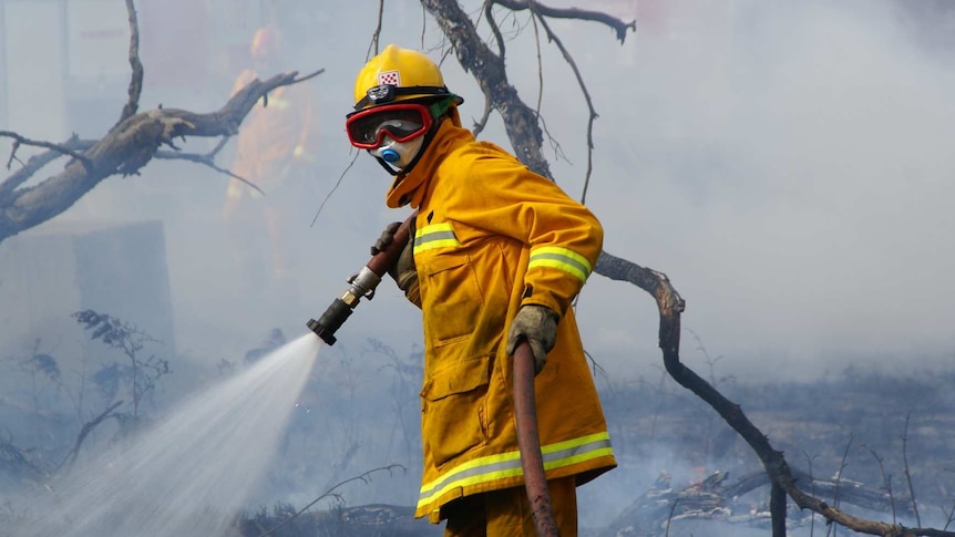 A CFA firefighter, wearing goggles and breathing mask and hose in smoky area.