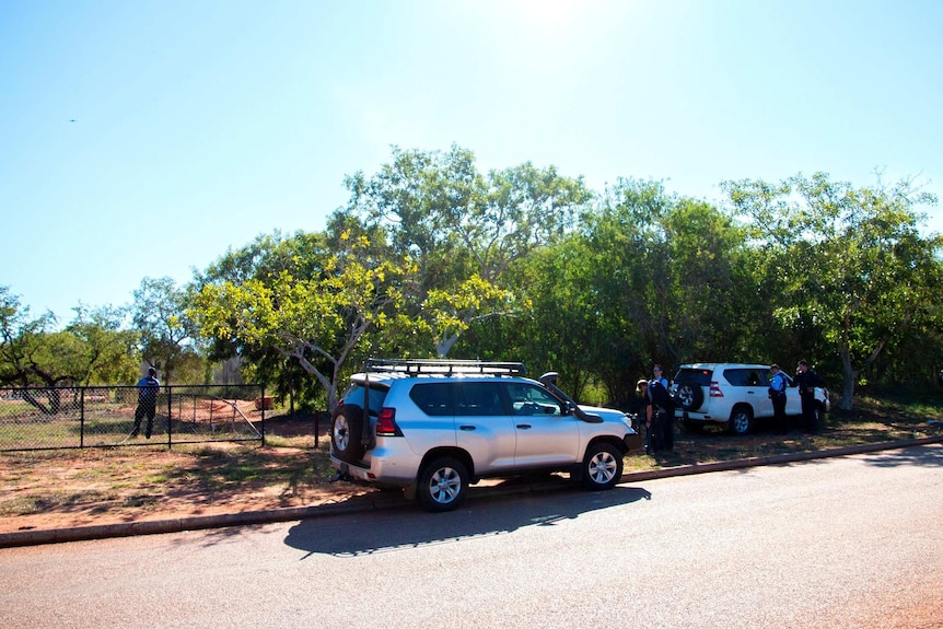 Two four-wheel drives parked on the side of the road with police officers standing nearby.