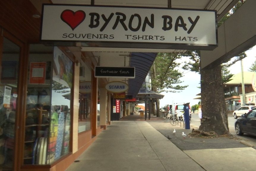 A footpath with shops and a sign with a love heart that says  'Byron Bay'