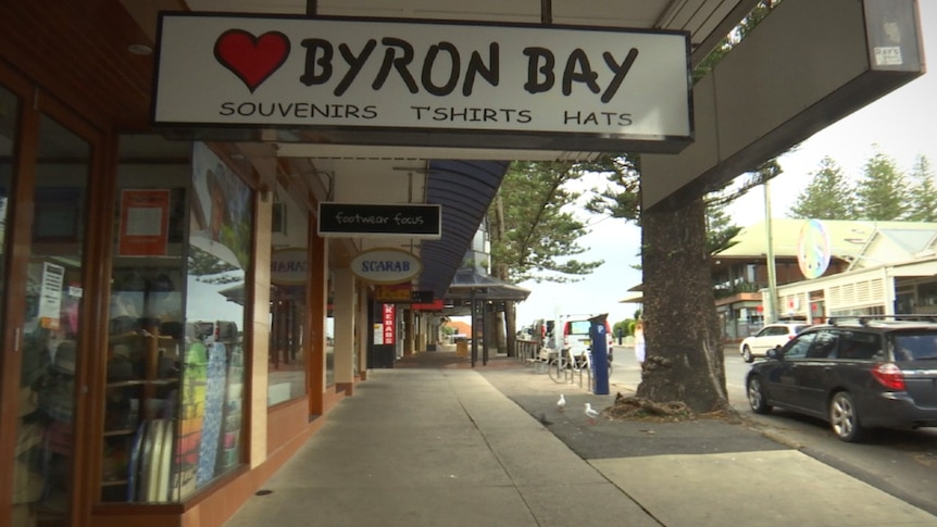 A footpath with shops and a sign with a love heart that says  'Byron Bay'
