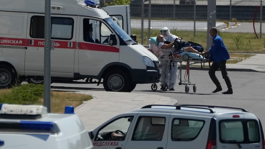 Two paramedics in full PPE wheel a stretcher carrying a man towards an ambulance