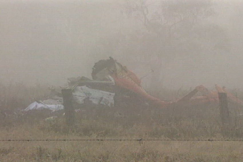 A helicopter destroyed in a crash in a foggy paddock.