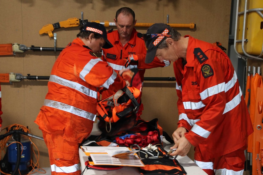 Three men are seen standing around a table in their orange SES gear.