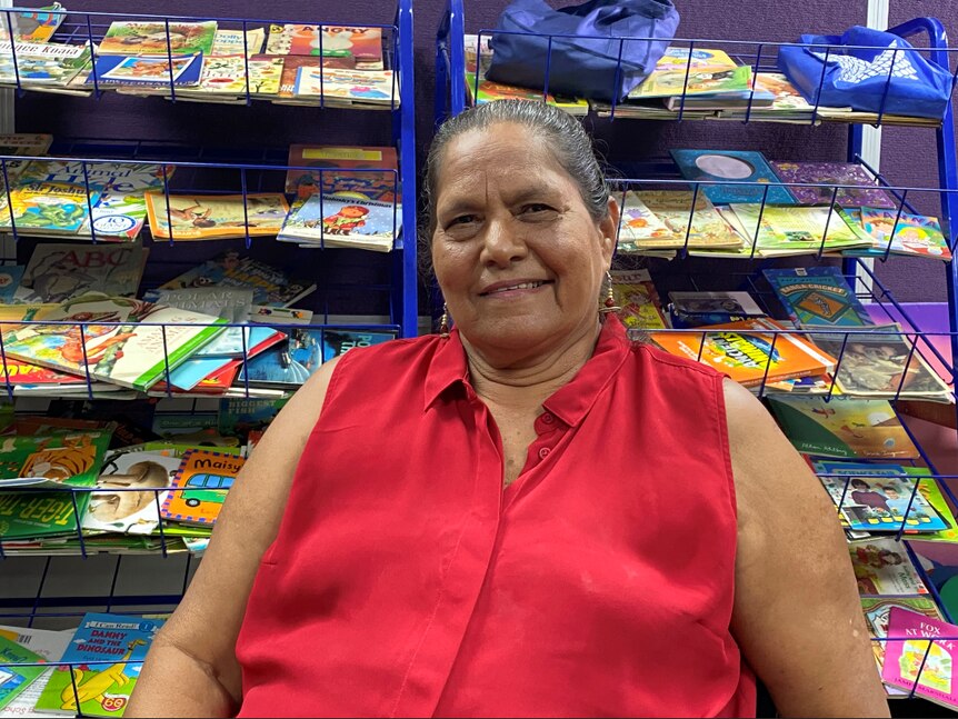 A woman sits in front of a set of bookshelves, smiling at the camera.